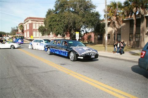 Blue race car leading a line of cars on a city street with spectators nearby