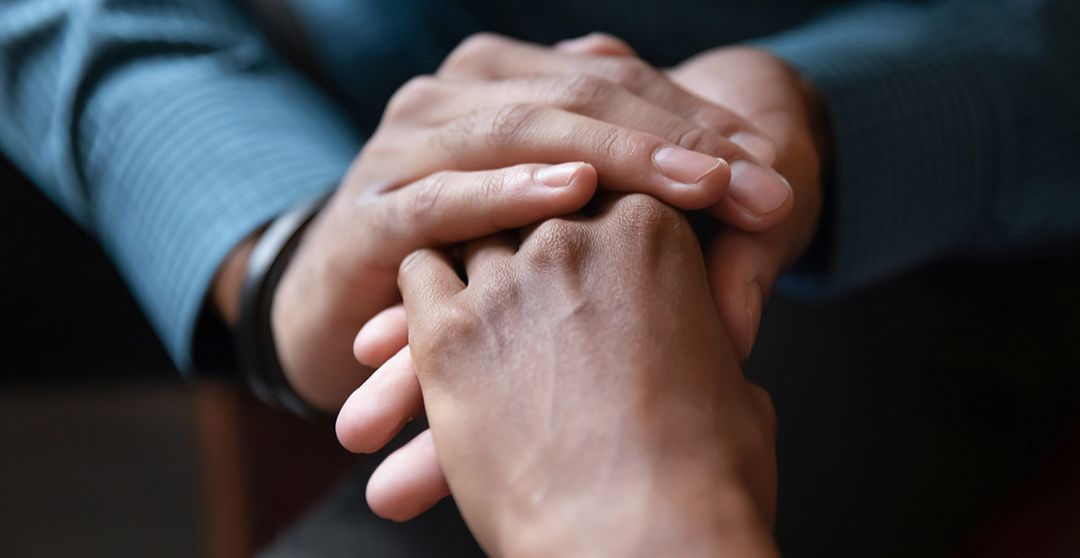 Two hands clasped together in a close-up, conveying support or comfort.