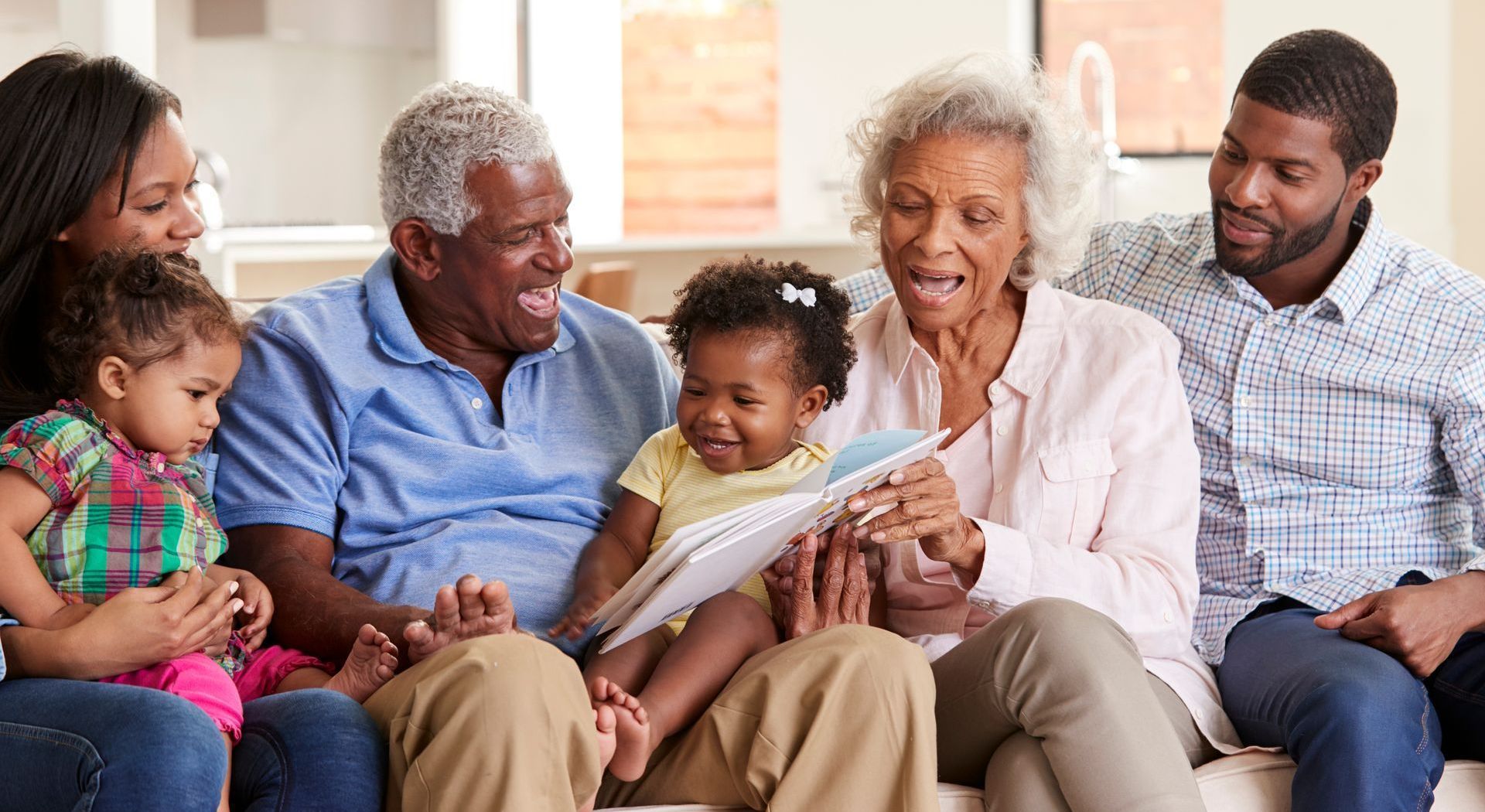 Family sitting together on a couch, smiling and interacting with a baby in a cozy living room.