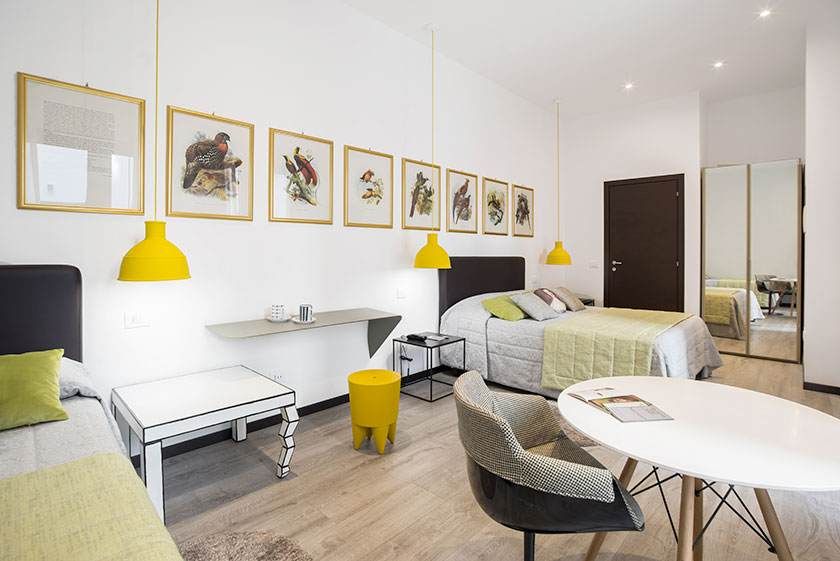 Dormitorio con dos camas, escritorio, lámparas amarillas, obras de arte y mesa redonda. Luminoso y moderno.