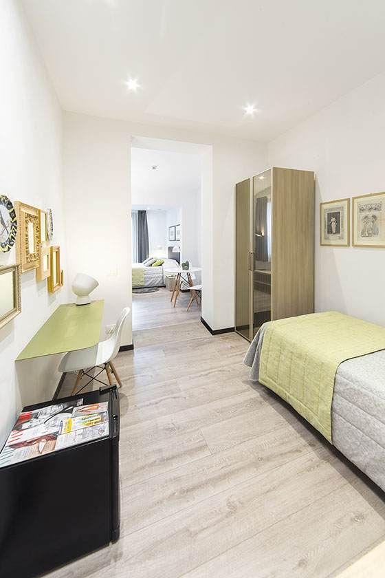 Dormitorio estrecho con suelos de madera clara, una cama individual y un escritorio.