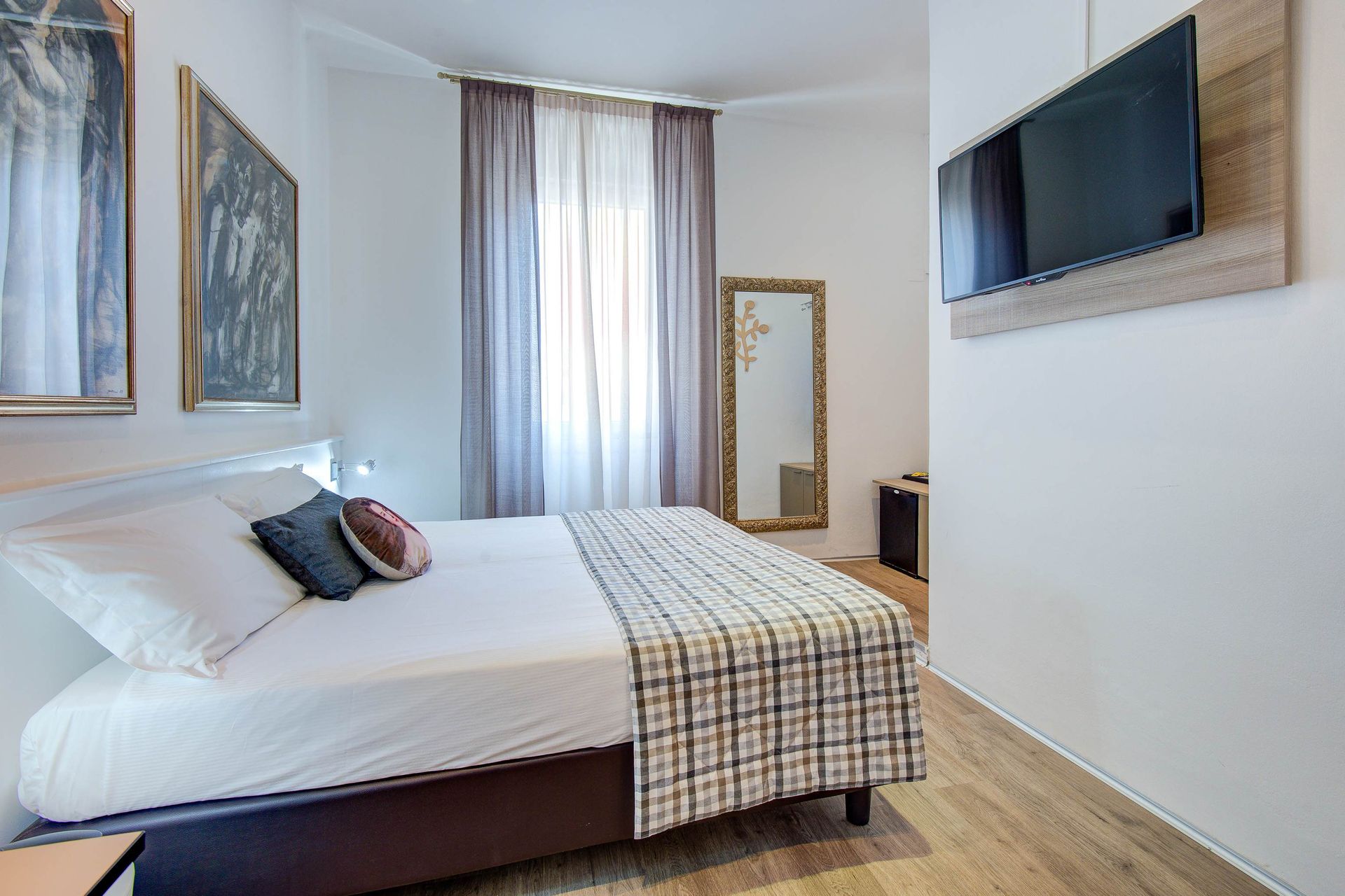 Dormitorio con cama, arte, espejo, cortinas y TV de pared.