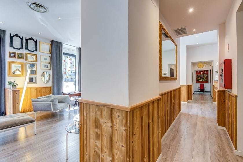 Pasillo interior con paneles de madera que conduce a otra habitación; se ven obras de arte y un sofá.