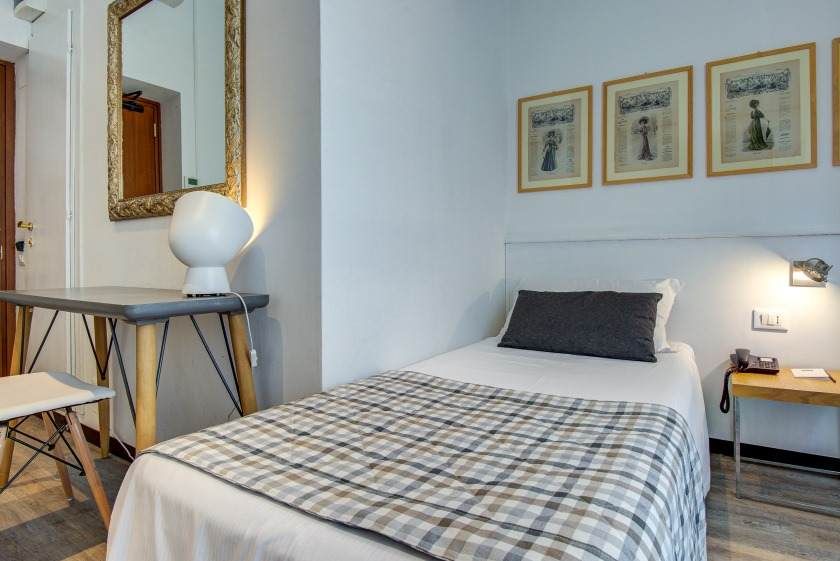 Pequeña habitación de hotel con una cama individual, escritorio, espejo y obras de arte en la pared.