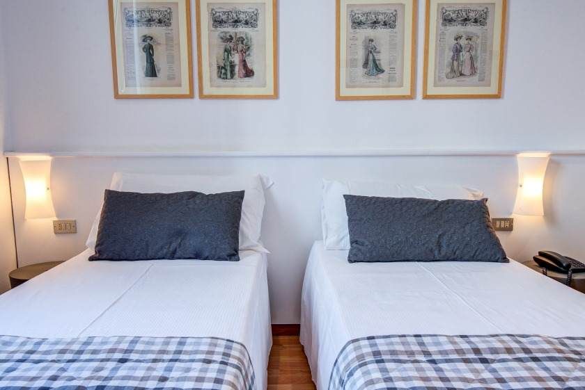 Dos camas individuales con sábanas blancas y almohadas grises. Obra de arte en la pared superior.