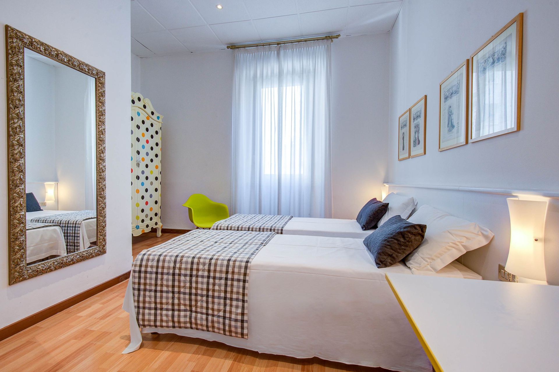 Dormitorio con dos camas individuales, espejo grande y obra de arte en una pared blanca.