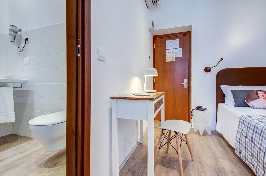 Habitación de hotel con escritorio, cama y puerta de baño abierta.