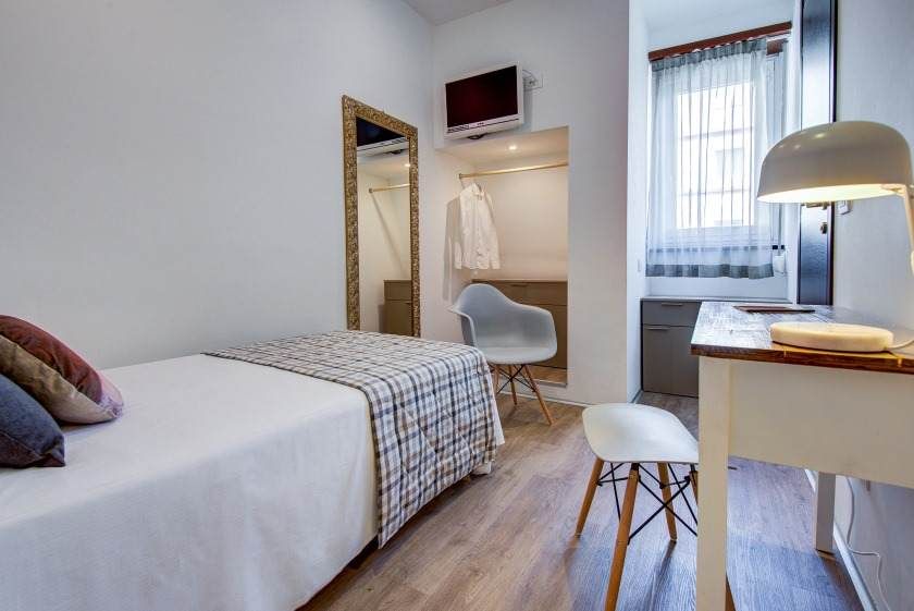 Pequeña habitación de hotel con cama individual, escritorio y armario.