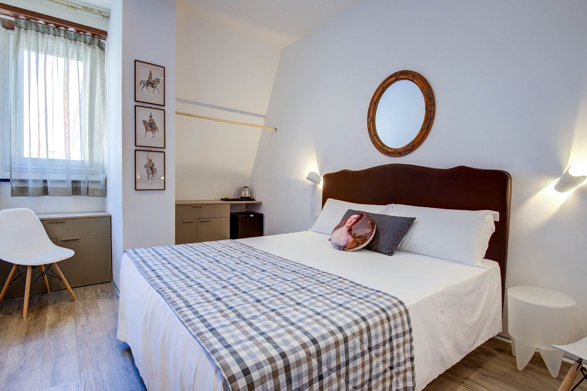 Dormitorio con cama, ventana, mesa auxiliar, obras de arte y paredes blancas.