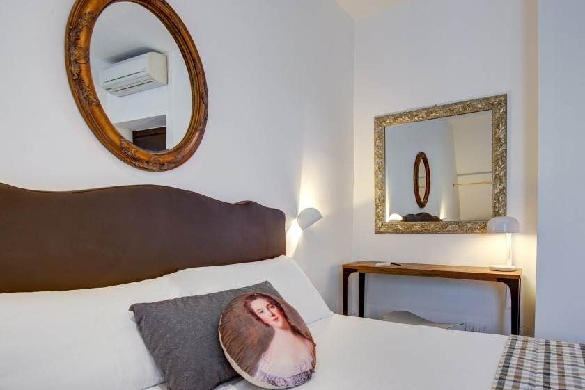 Dormitorio con cama, almohadas, espejos y mesa auxiliar.