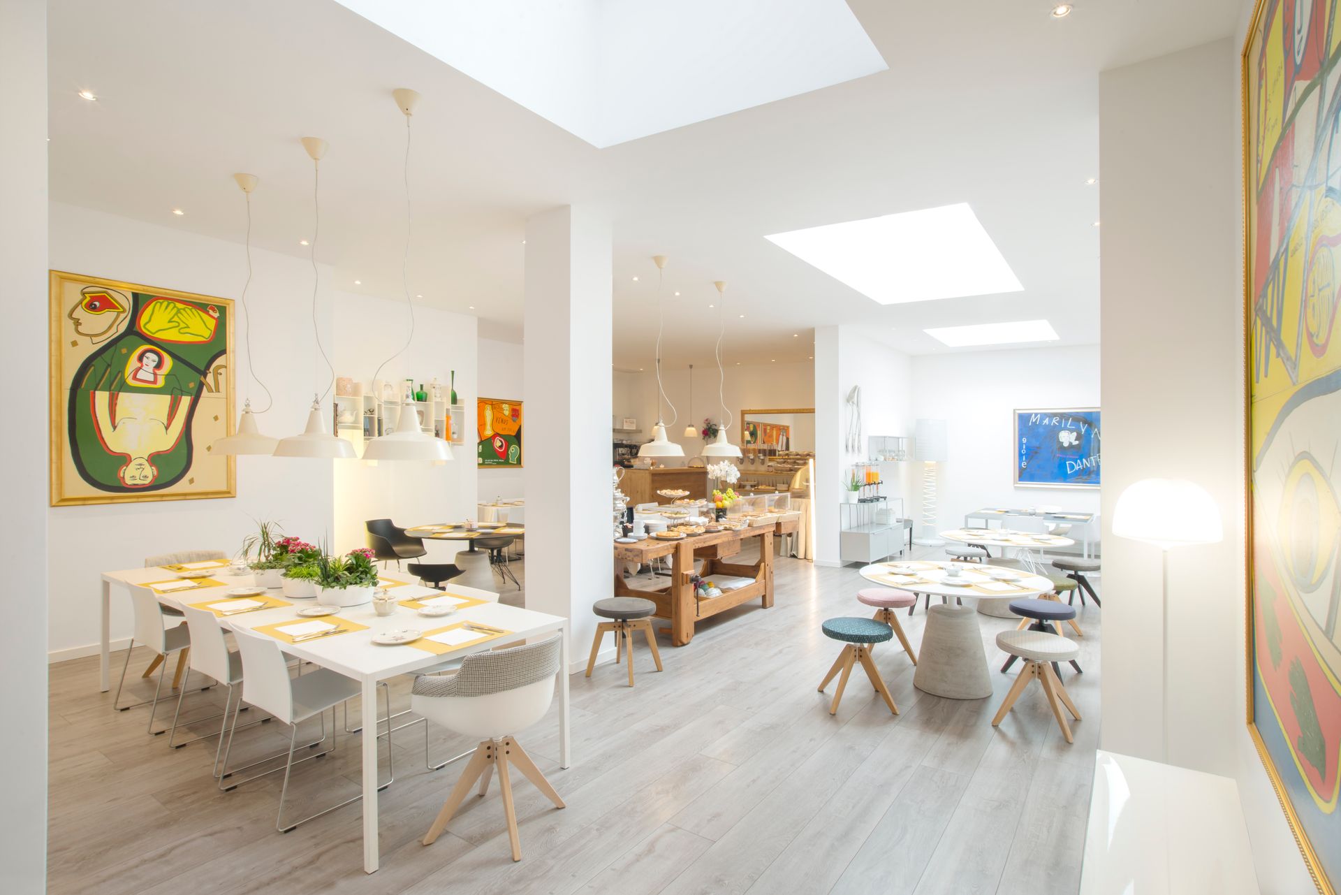 Estudio de arte amplio y luminoso con varias mesas, obras de arte y lámparas colgantes.