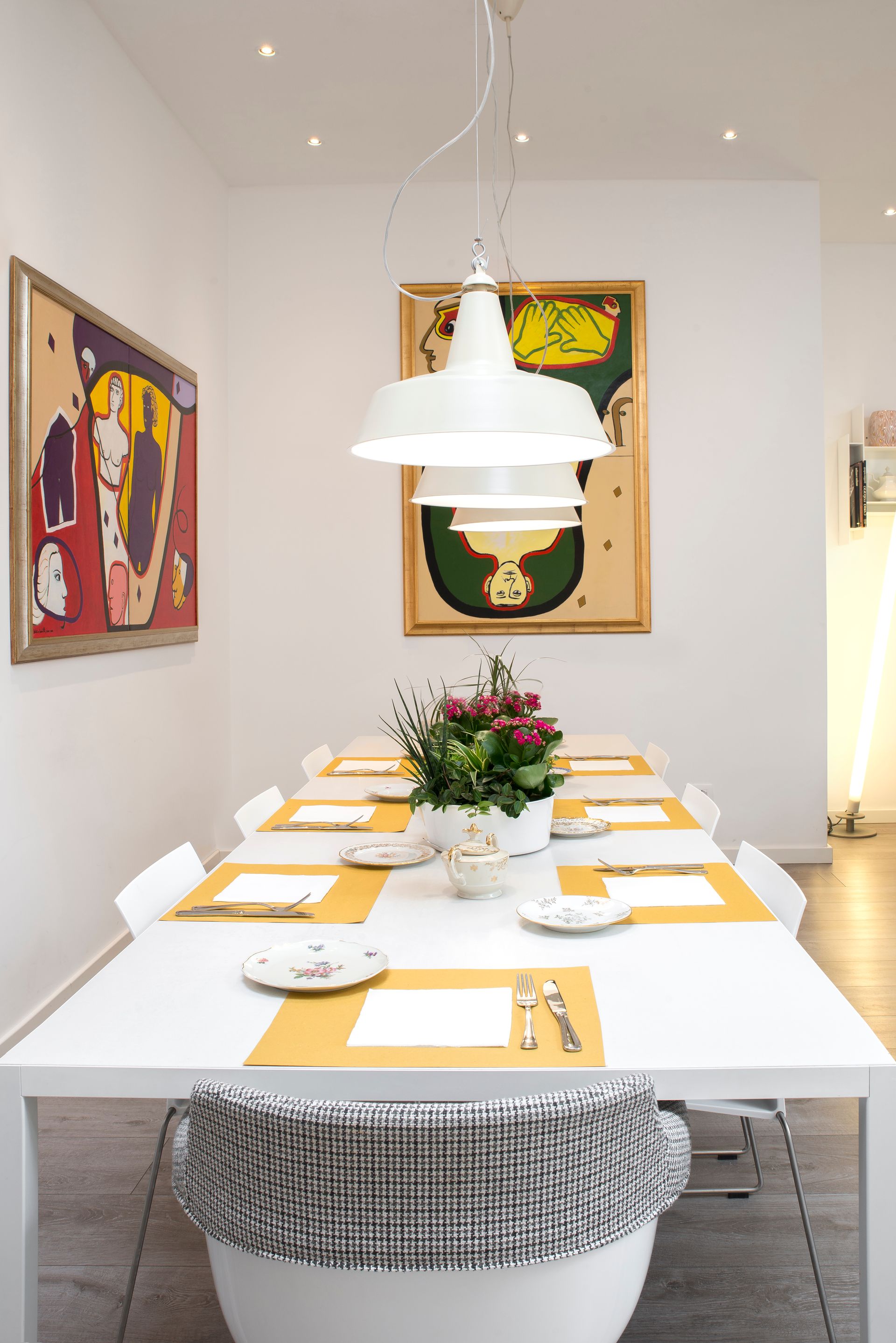 Comedor formal: mesa blanca, cubiertos para ocho personas, arte en las paredes, luces colgantes blancas.