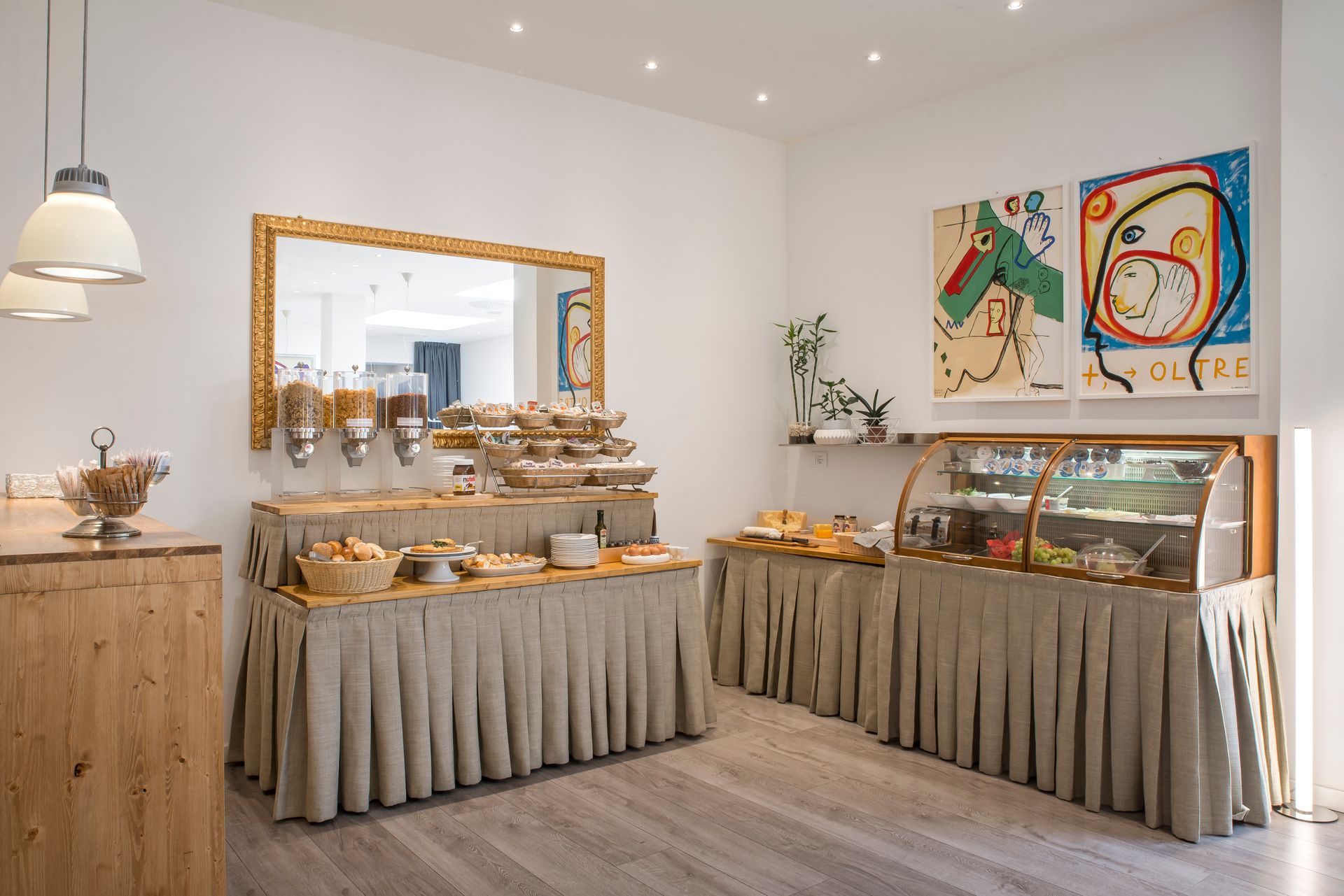 Buffet servido en sala luminosa con cereales, bollería y vitrina refrigerada.