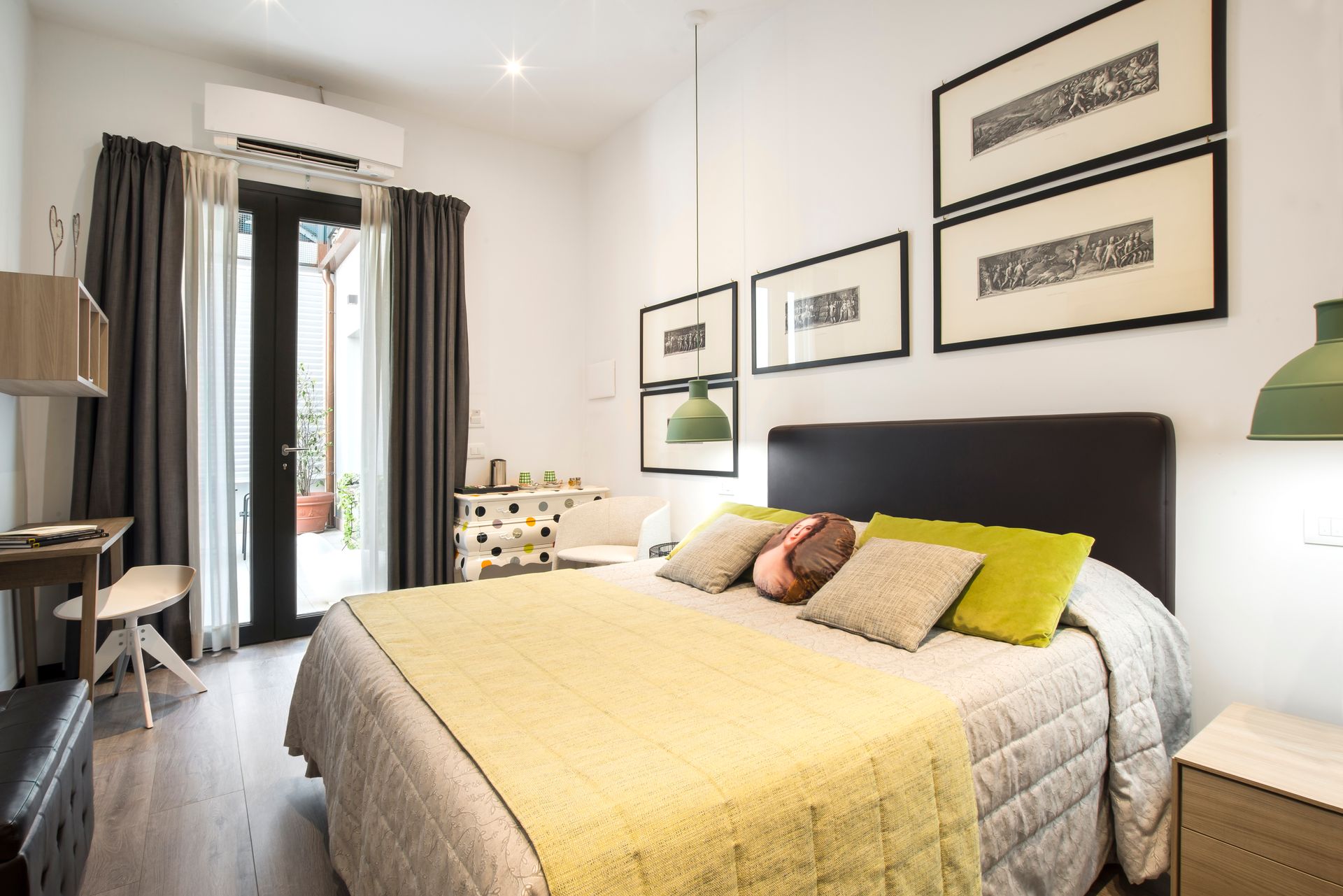 Dormitorio con cama, edredón amarillo, arte enmarcado y puerta de entrada a un patio.