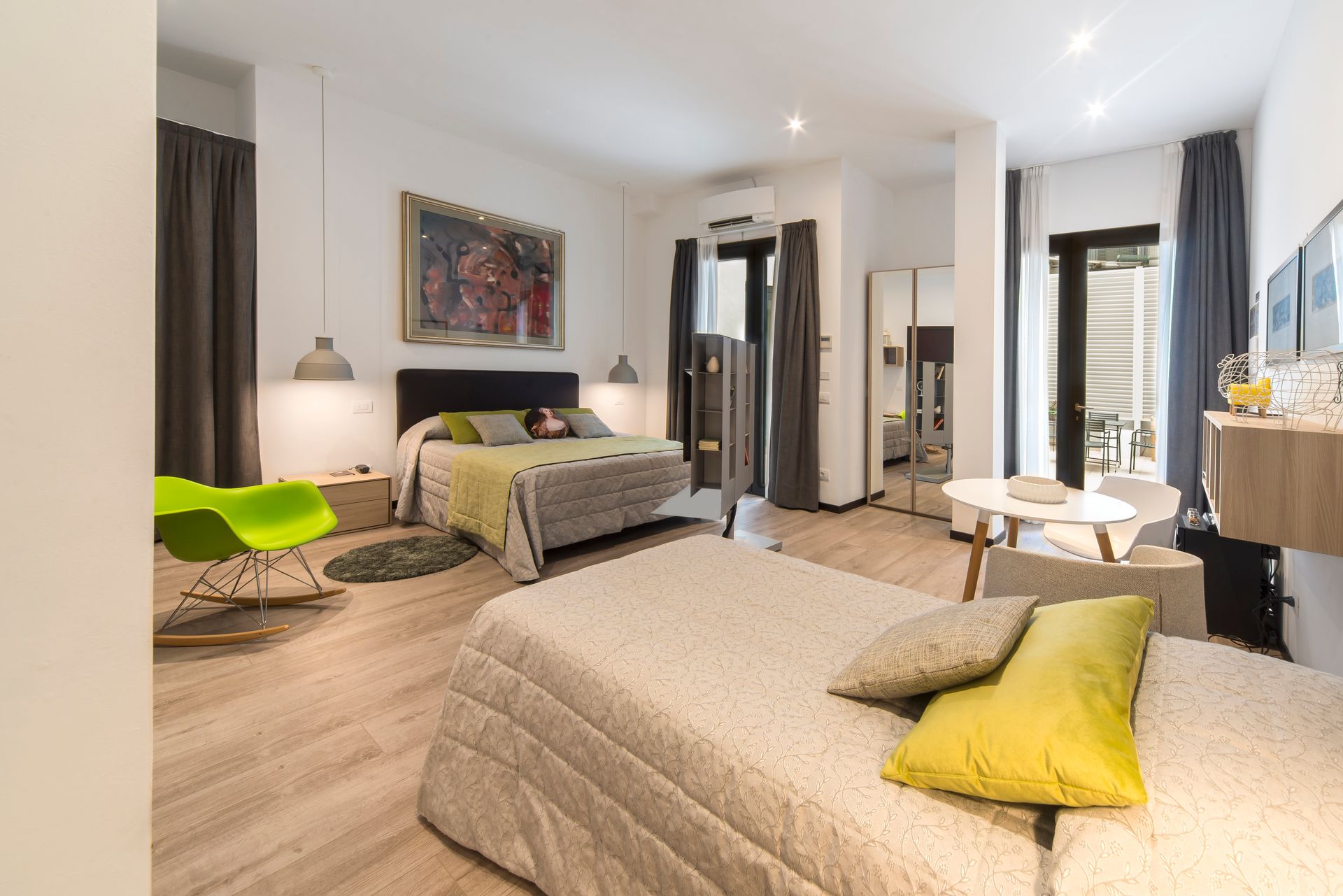 Dormitorio con dos camas, almohadas amarillas, silla verde, paredes blancas y suelo de madera.