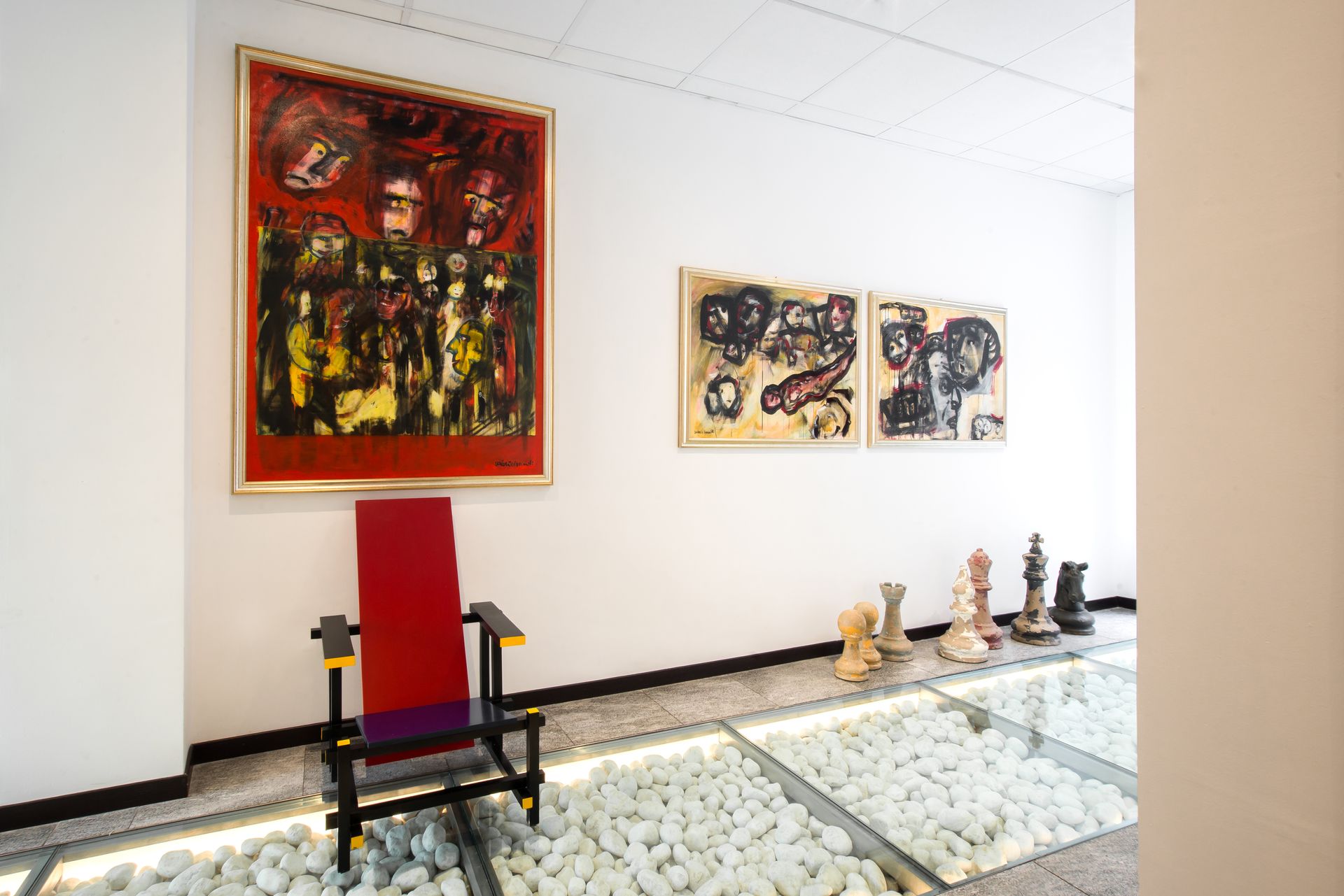 Una silla roja se encuentra debajo de una obra de arte sobre una pared blanca en un espacio de galería.