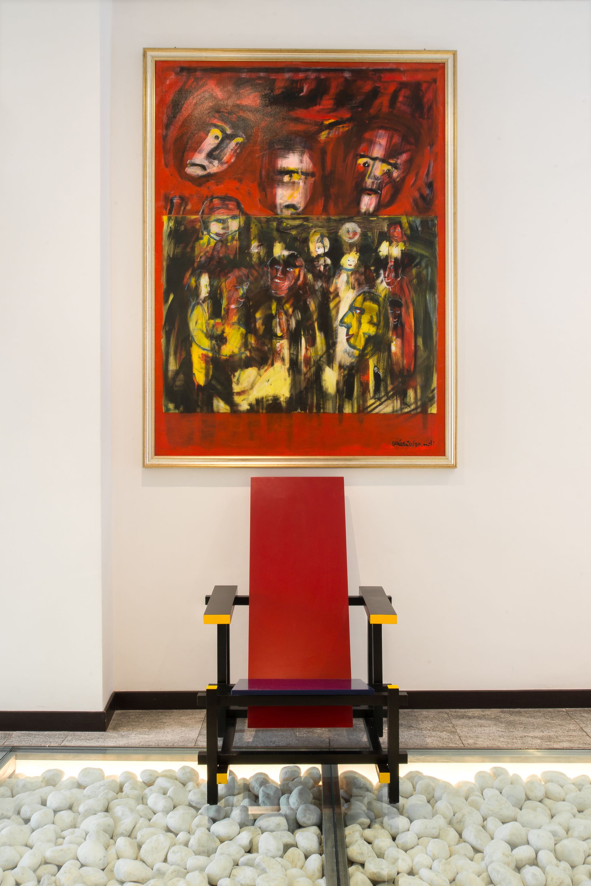 Silla roja estilo Mondrian debajo de una pintura abstracta colorida sobre una pared blanca.