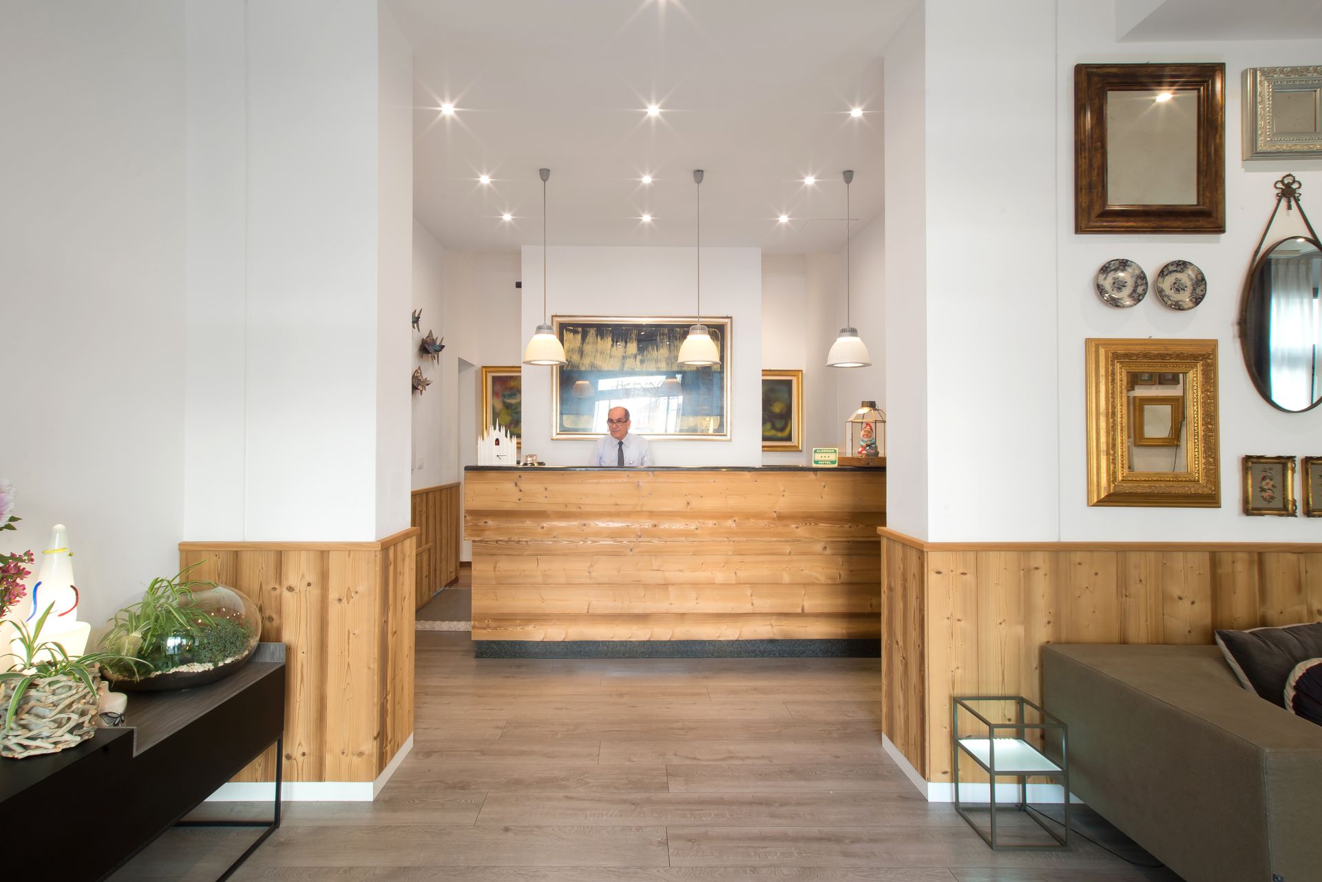 Vestíbulo del hotel con mostrador de recepción de madera y varias obras de arte enmarcadas en la pared.