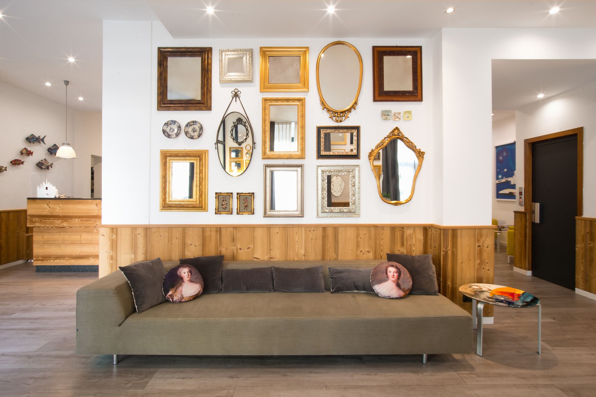 Un sofá con cojines frente a una pared con varios espejos. Se ven detalles de madera, un escritorio y una puerta.