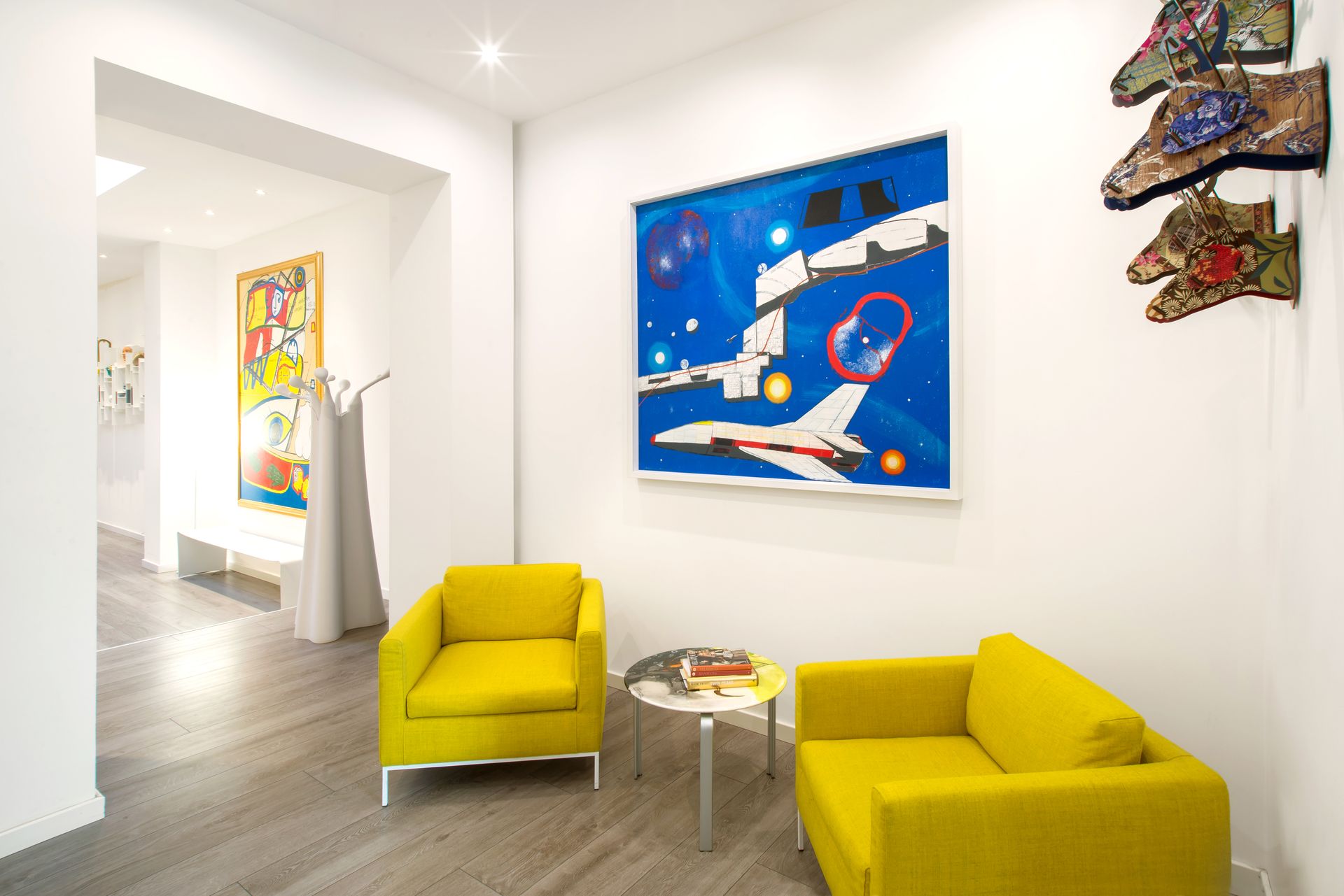 Una entrada luminosa a una galería de arte con sillas amarillas, obras de arte y un pasillo que conduce a otras salas.