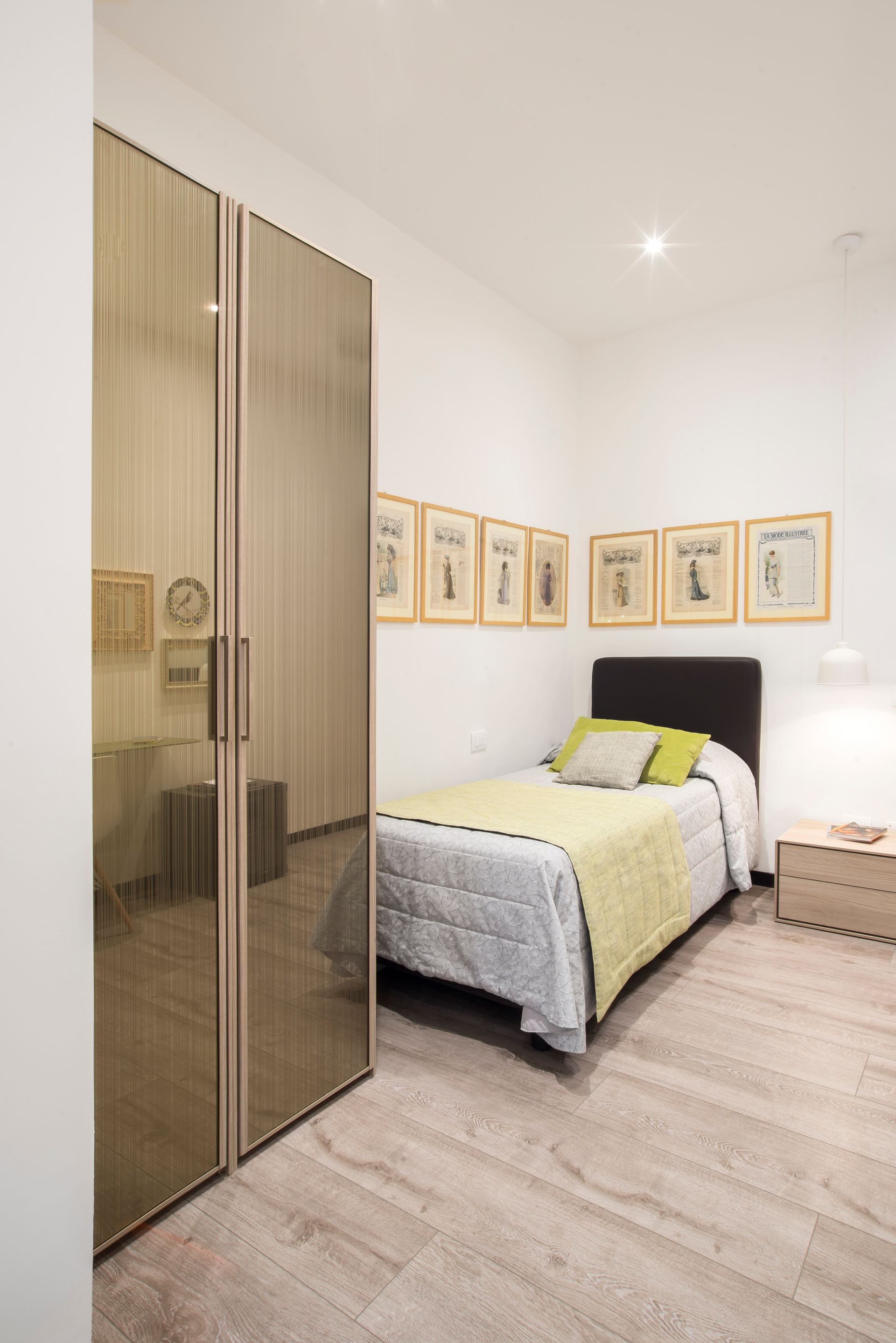 Dormitorio con cama, láminas artísticas, armario con espejo y suelo de madera.