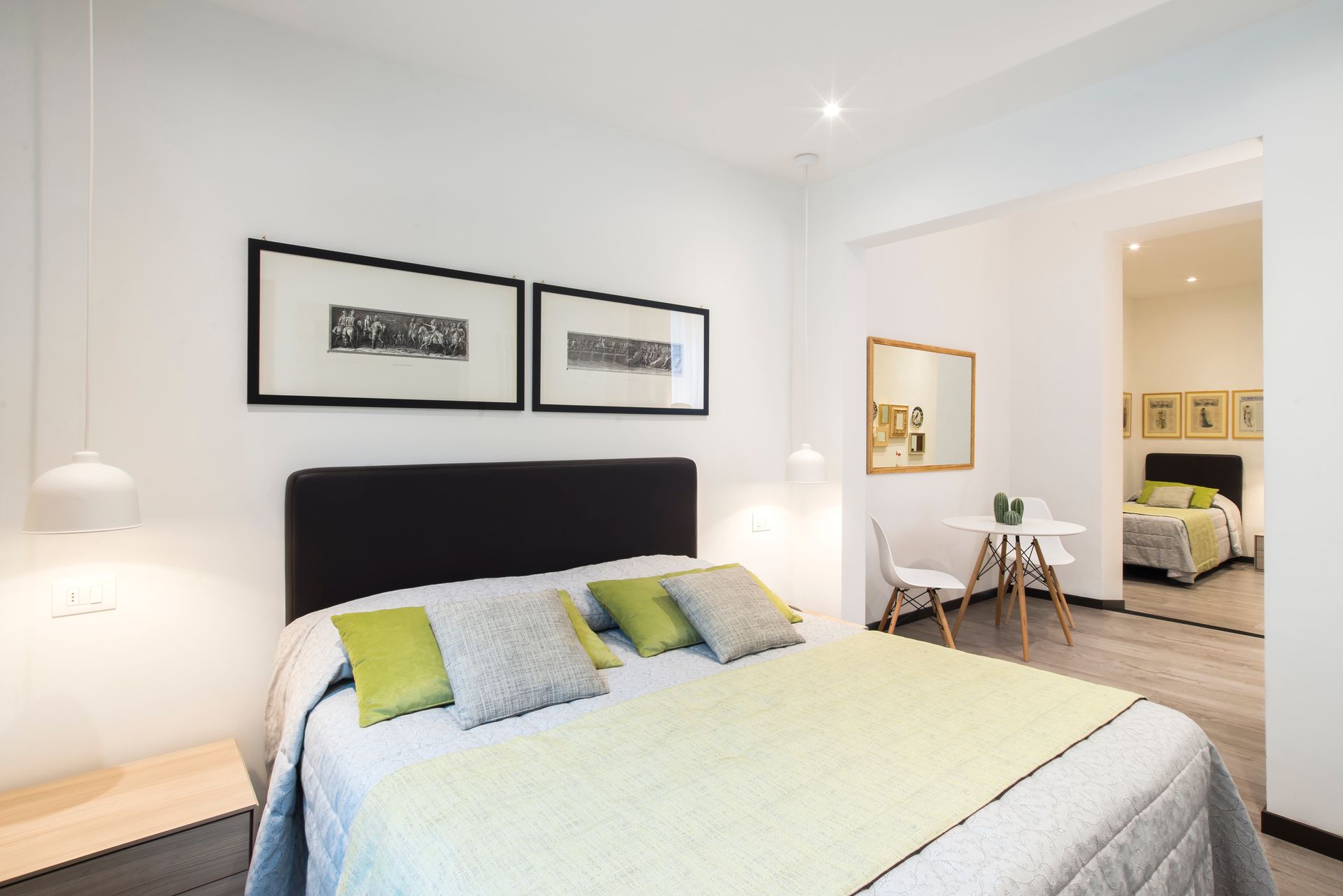 Dormitorio con cama, almohadas, obras de arte, mesa y una vista de otra habitación.