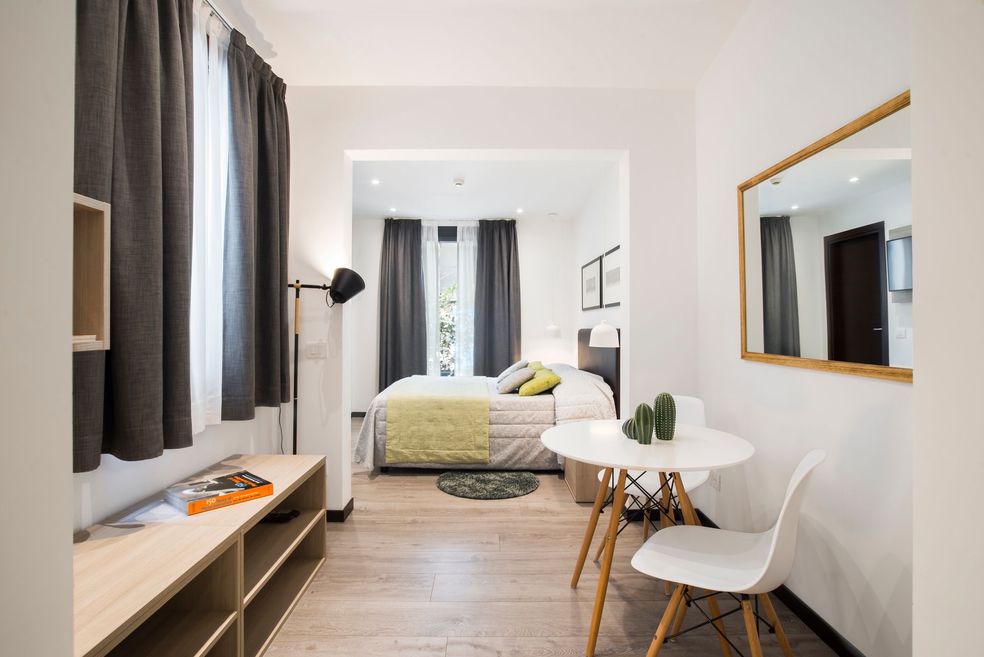 Dormitorio con cama, mesa, sillas, espejo y cortinas en un espacio moderno y luminoso.