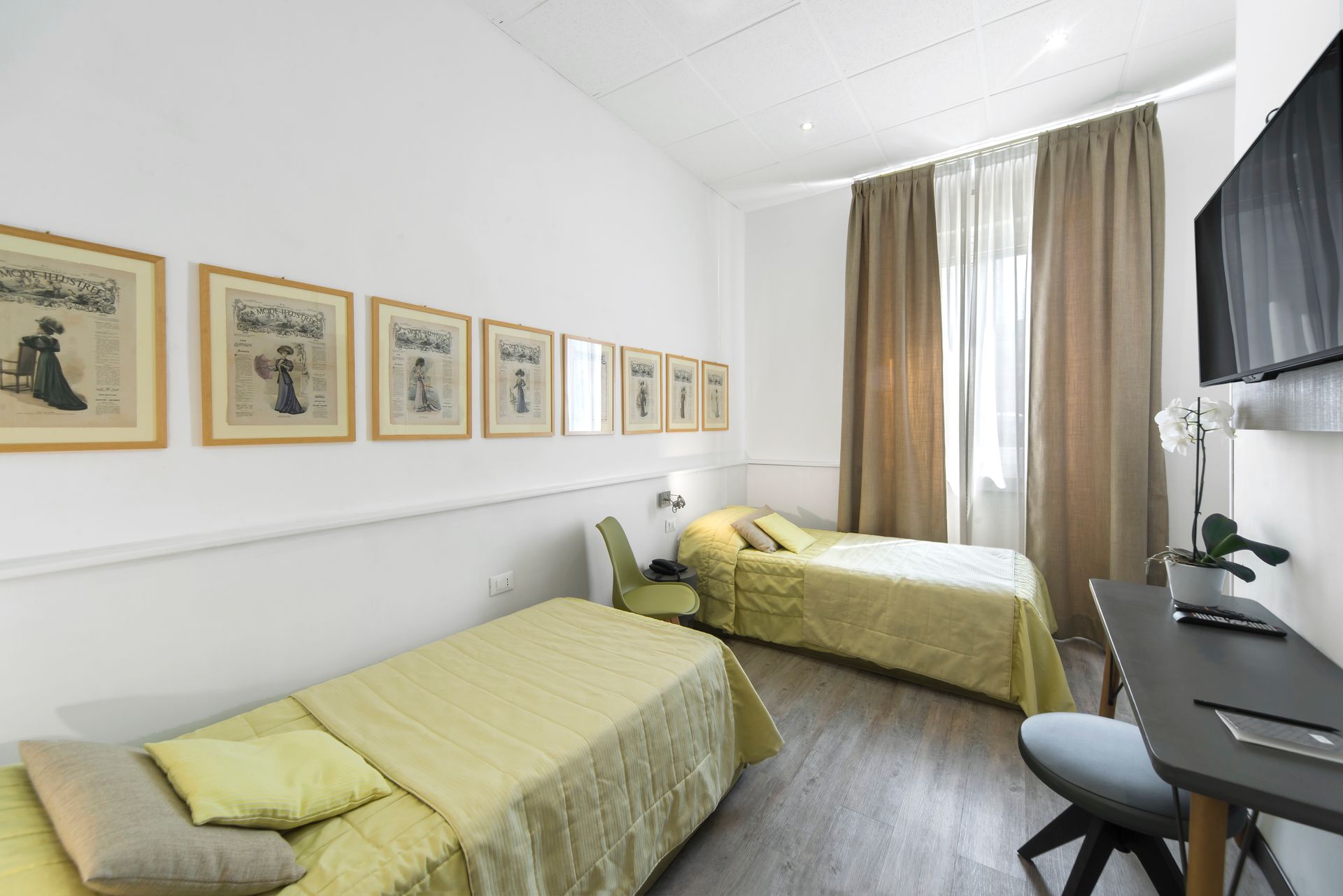 Habitación de hotel con dos camas individuales, escritorio, TV, obras de arte y combinación de colores neutros.