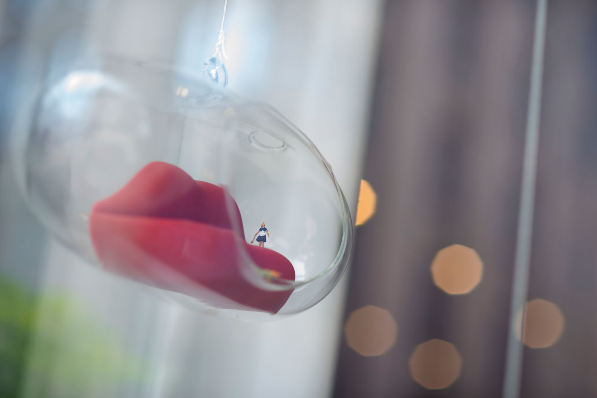 Escultura de labios rojos dentro de un recipiente colgante de vidrio transparente. Luces bokeh de fondo.
