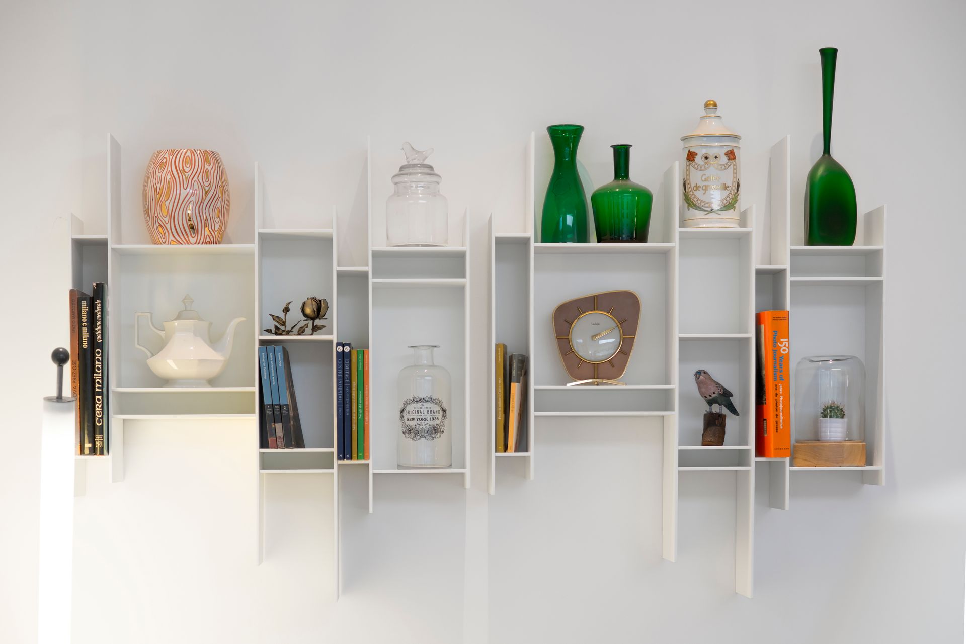 Estantes de pared modernos blancos que contienen libros, jarrones y objetos decorativos sobre una pared blanca.