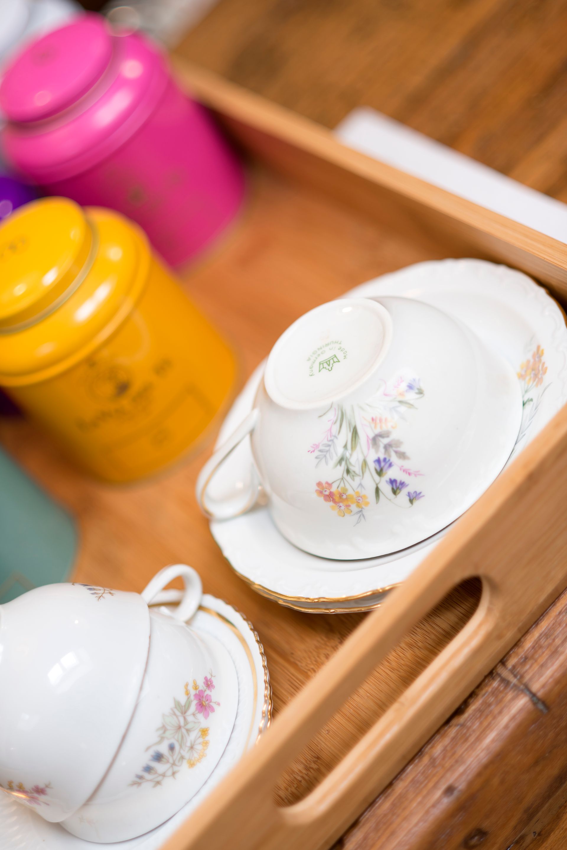 Bandeja de madera con tazas de té y platillos, junto a latas de té amarillas y rosas.