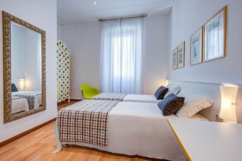 Twin beds in a bright room with a mirror, window, and decorative screen.