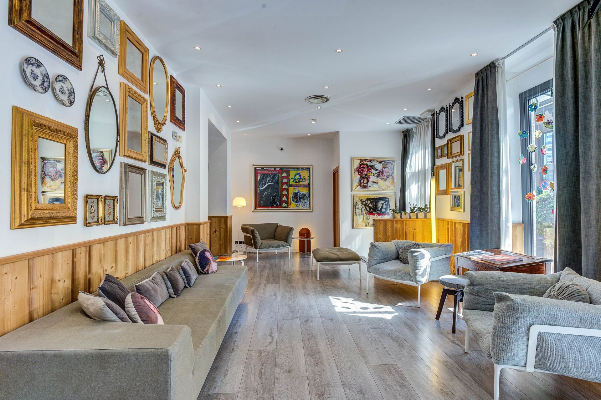 A modern living room with a long sofa, art gallery wall, light wood flooring, and large windows.