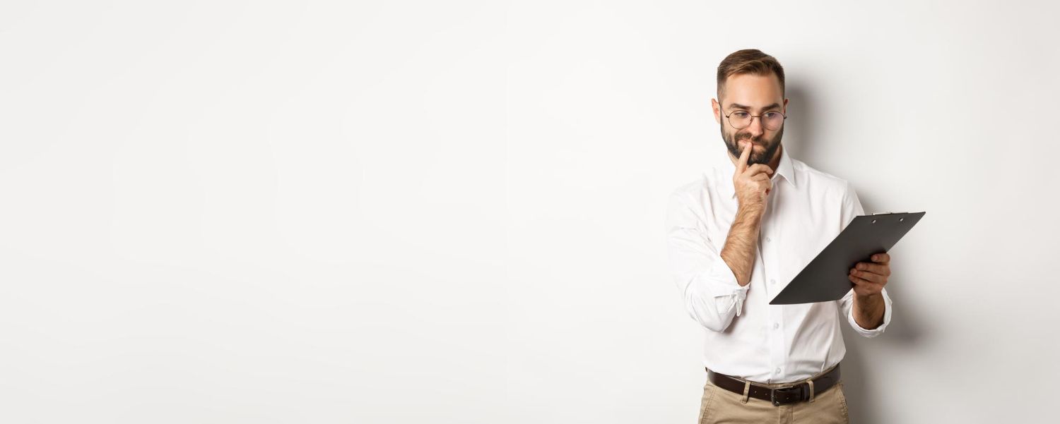Man holding a clipboard, looking thoughtful, finger on his chin, against a white background.
