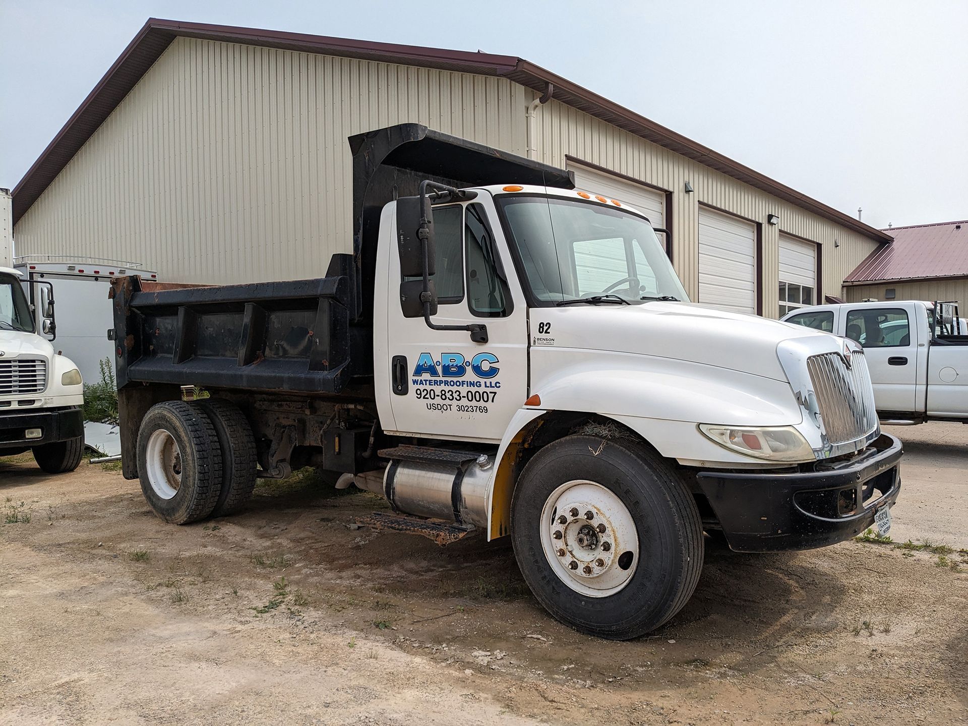 White dump truck parked in front of a building with garage doors.