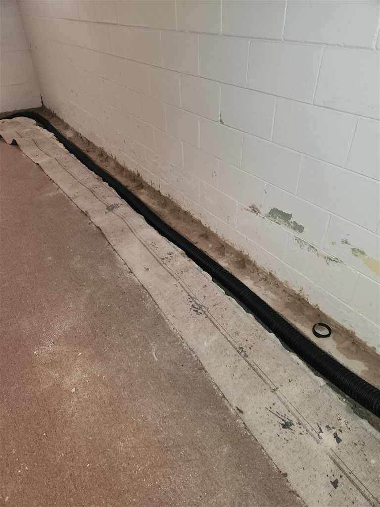 Basement with a long, black drain along the wall. 