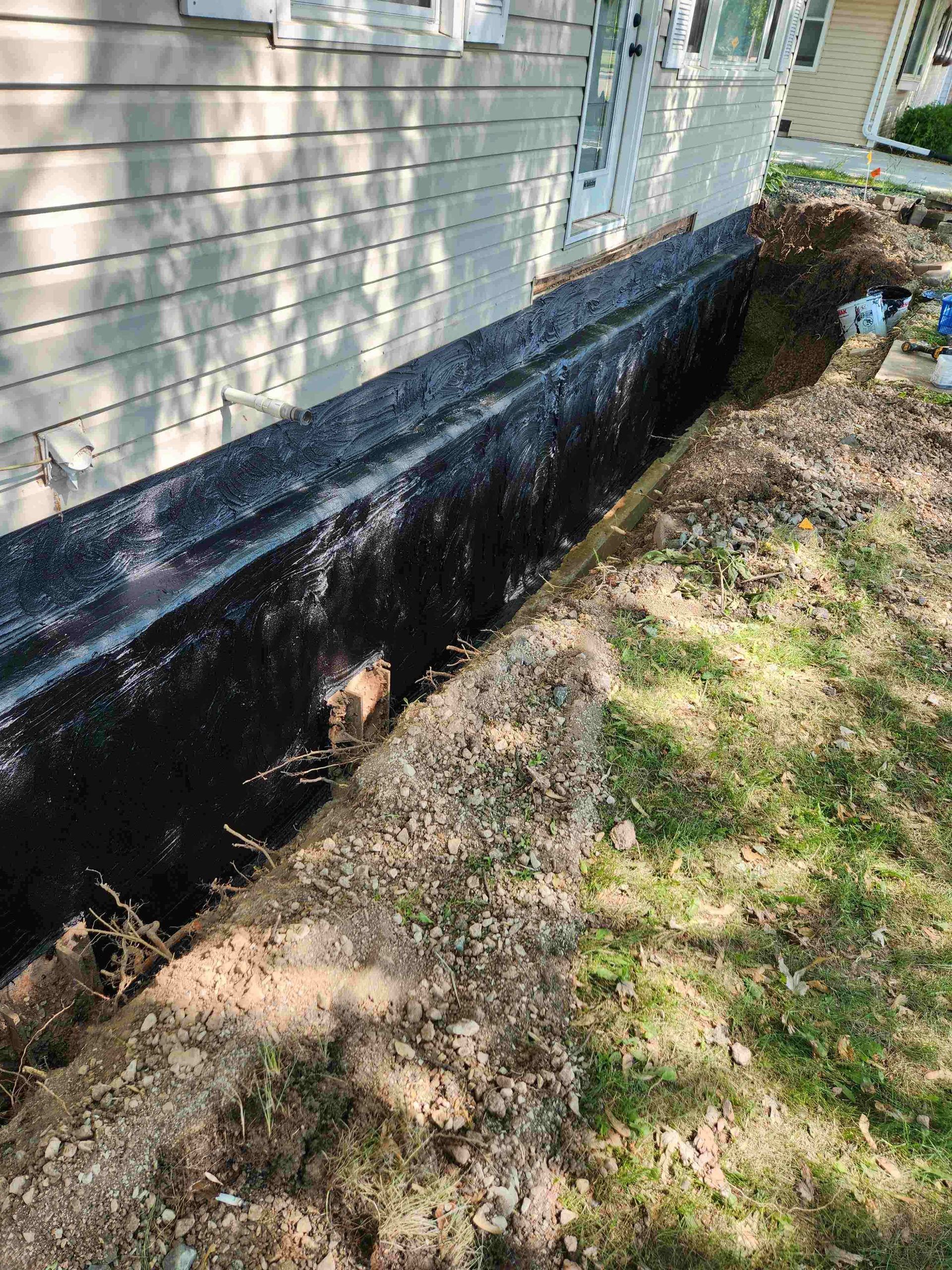 Exterior of a house with foundation being worked on; a trench is dug along the side of the building.