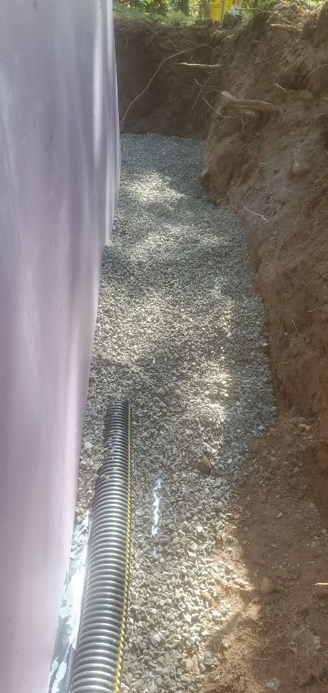 A trench filled with gravel, next to a pink wall, with a corrugated pipe running along the bottom.