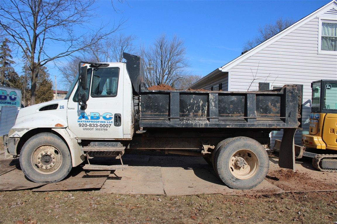 White dump truck parked on concrete, next to a house, on a sunny day.
