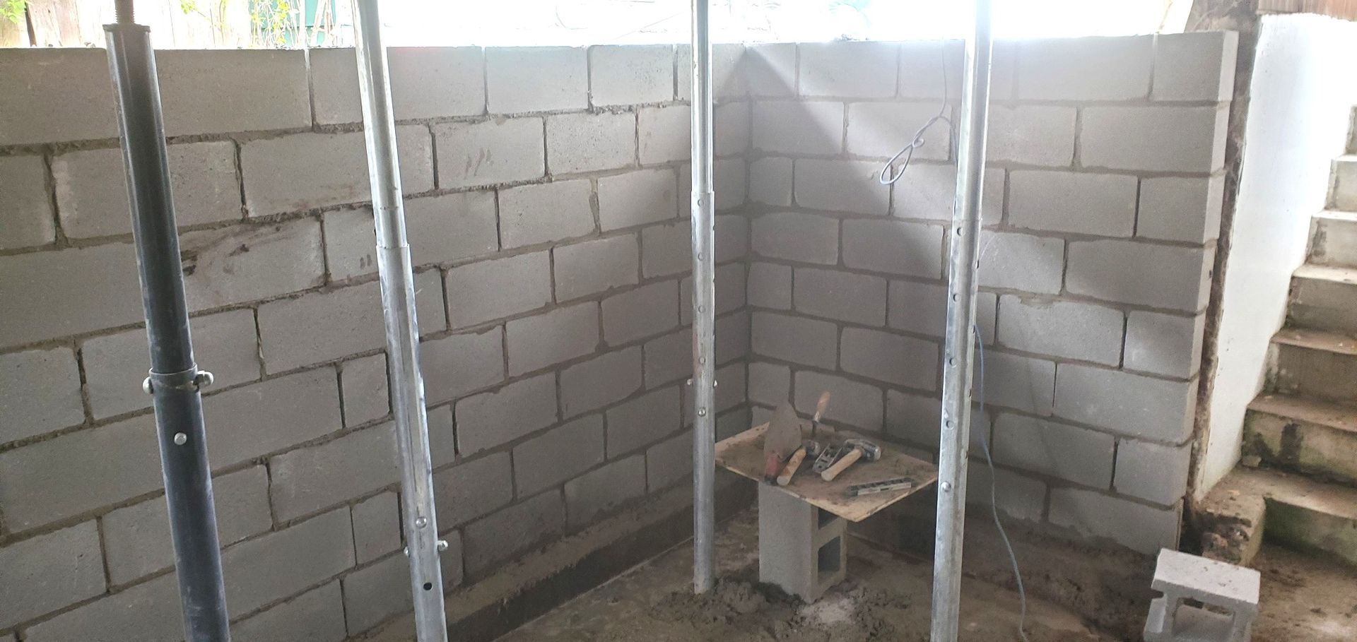 Construction site with cinder block walls and supporting metal poles. 