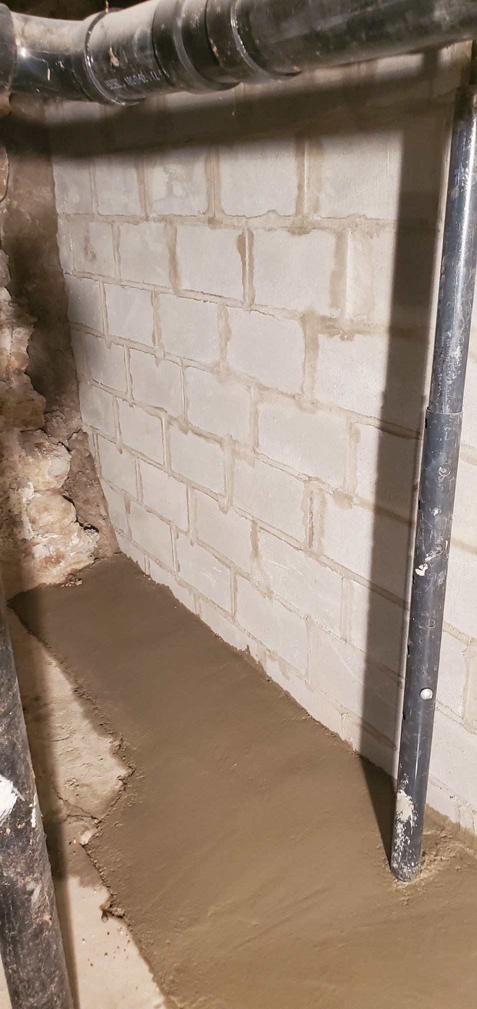 Concrete block wall with newly poured concrete floor, pipes in view.