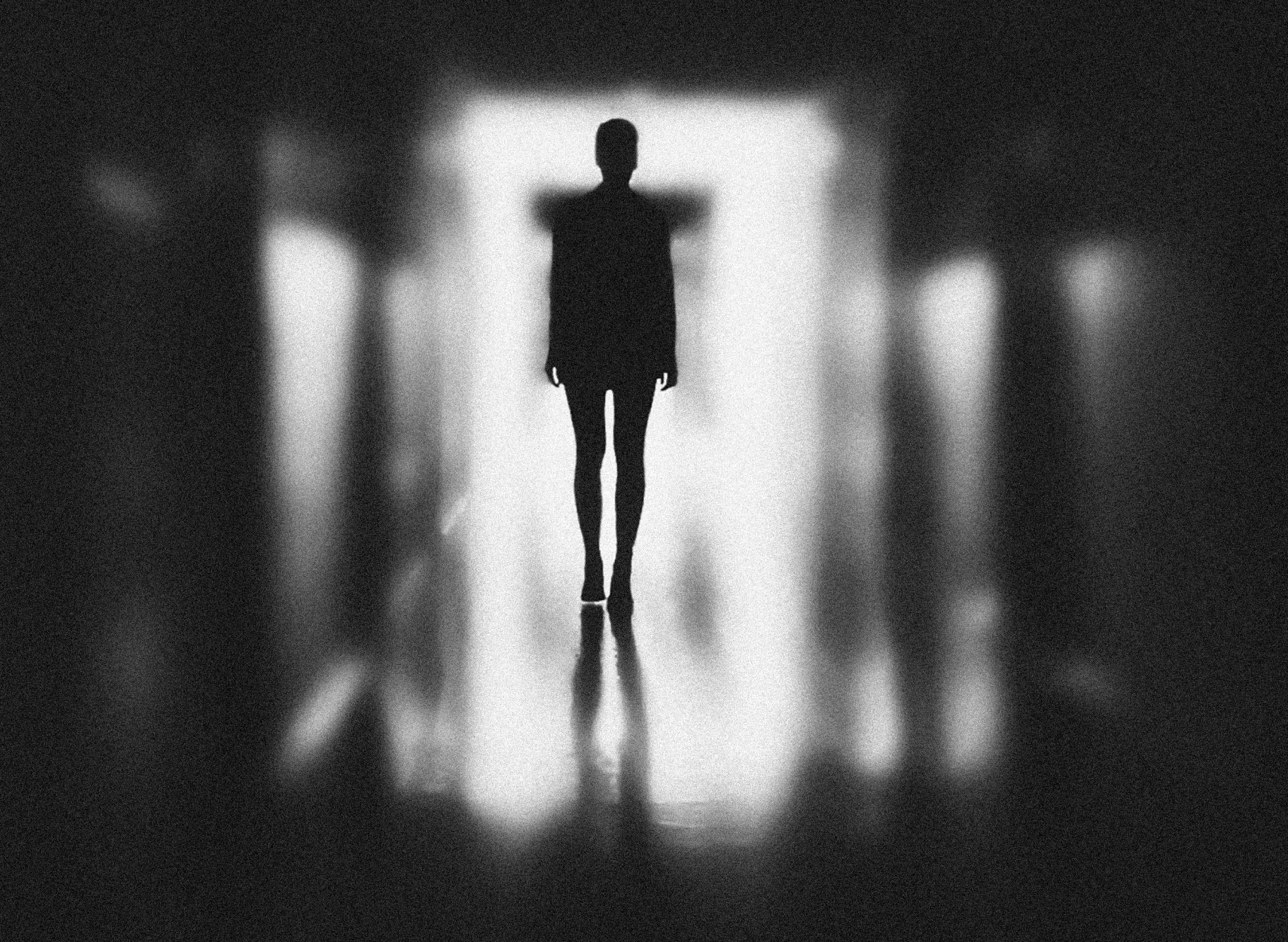 Silhouette of a person walking towards bright light at the end of a dark corridor.
