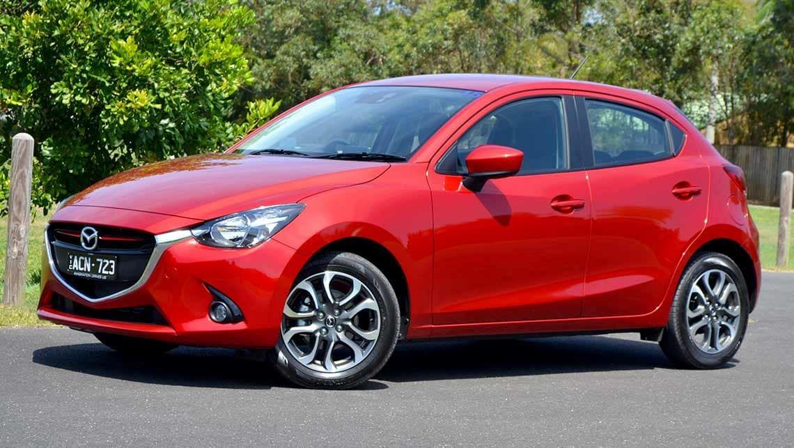 Red hatchback car parked on a road with trees in the background