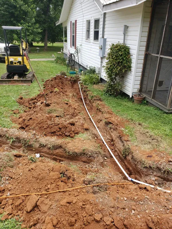 A yellow bulldozer is digging a hole in the dirt in front of a house.