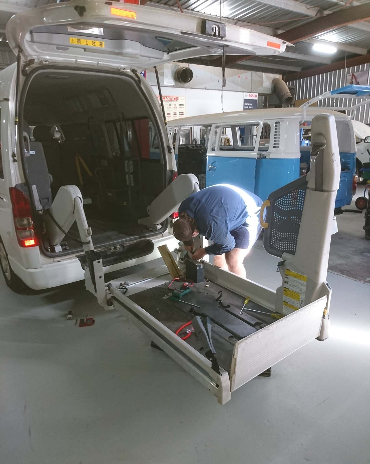 A Man Is Working On A Lift In The Back Of A Van — KC Auto Electrics In Ciccone, NT