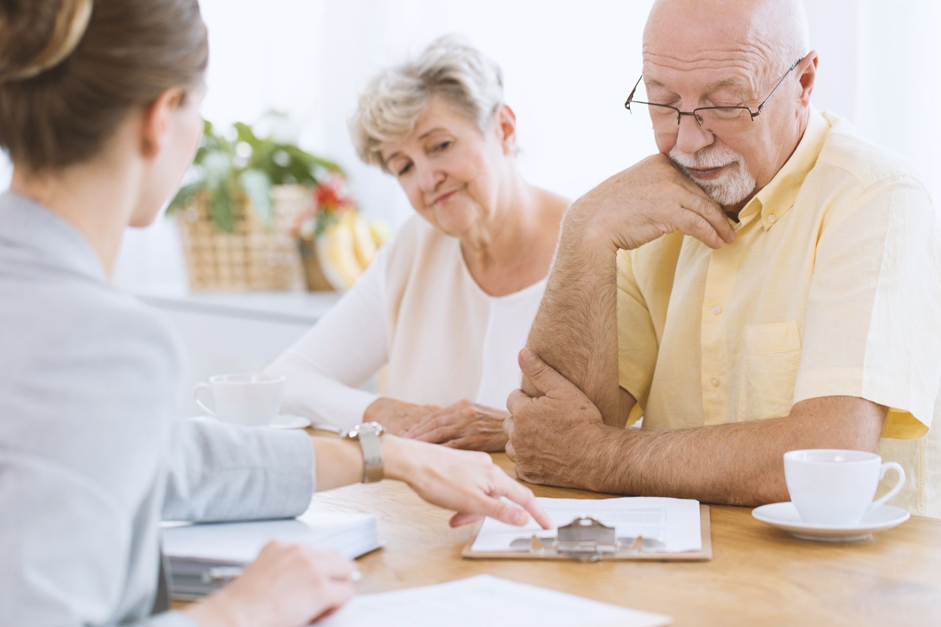Person consulting with two seniors at a table, pointing at documents in a bright office