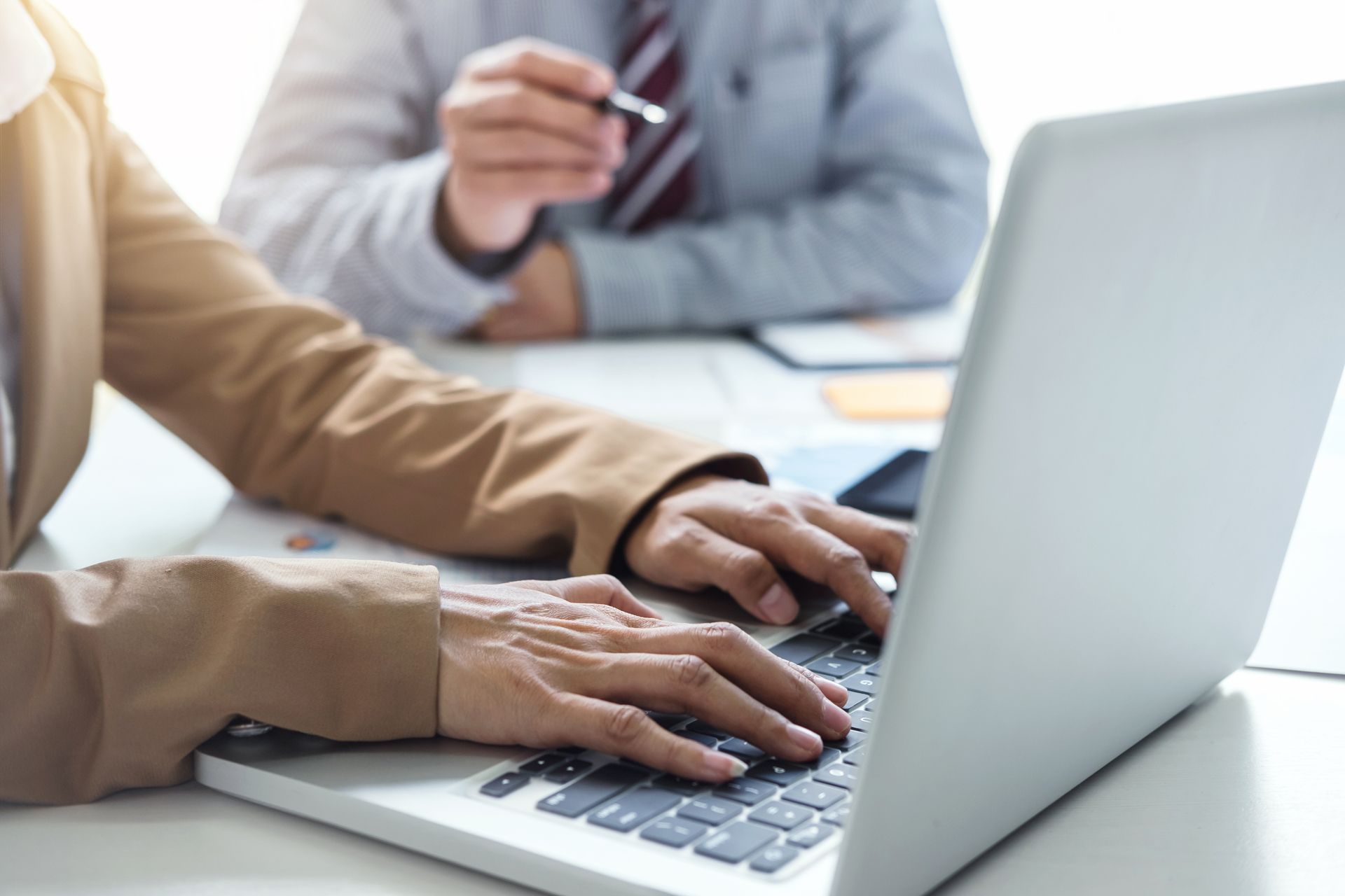 Person typing on a laptop while another person looks on in the background.