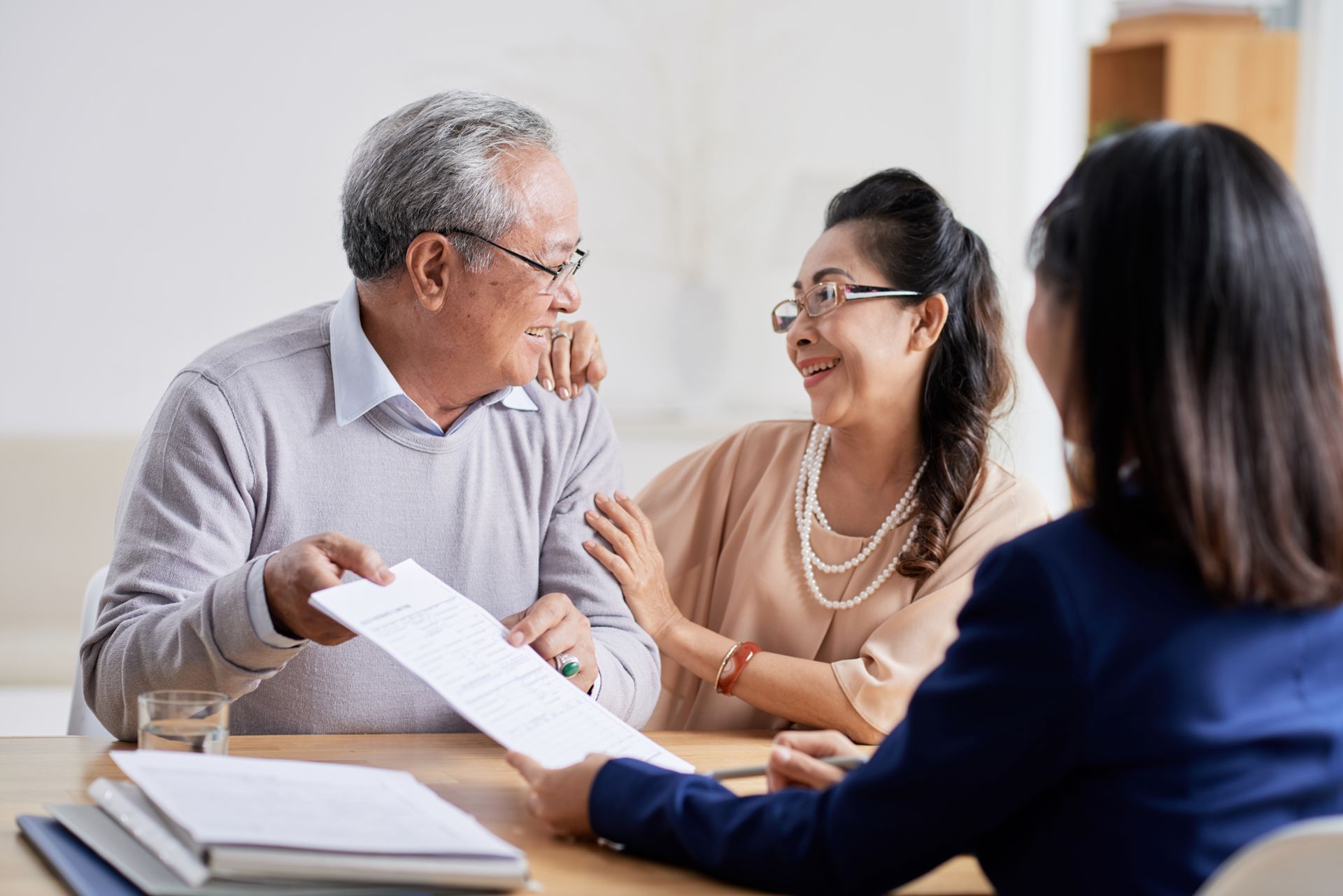 Three people discussing papers at a table in a bright office