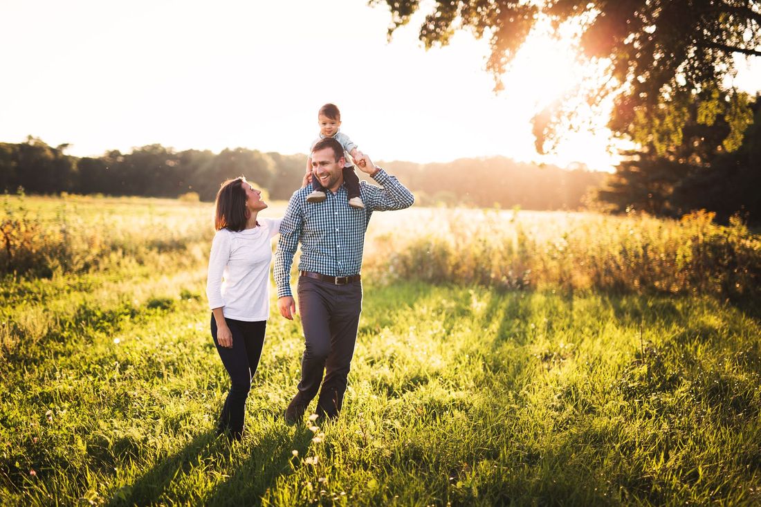 Family walking hand in hand through a sunlit grassy field at sunset