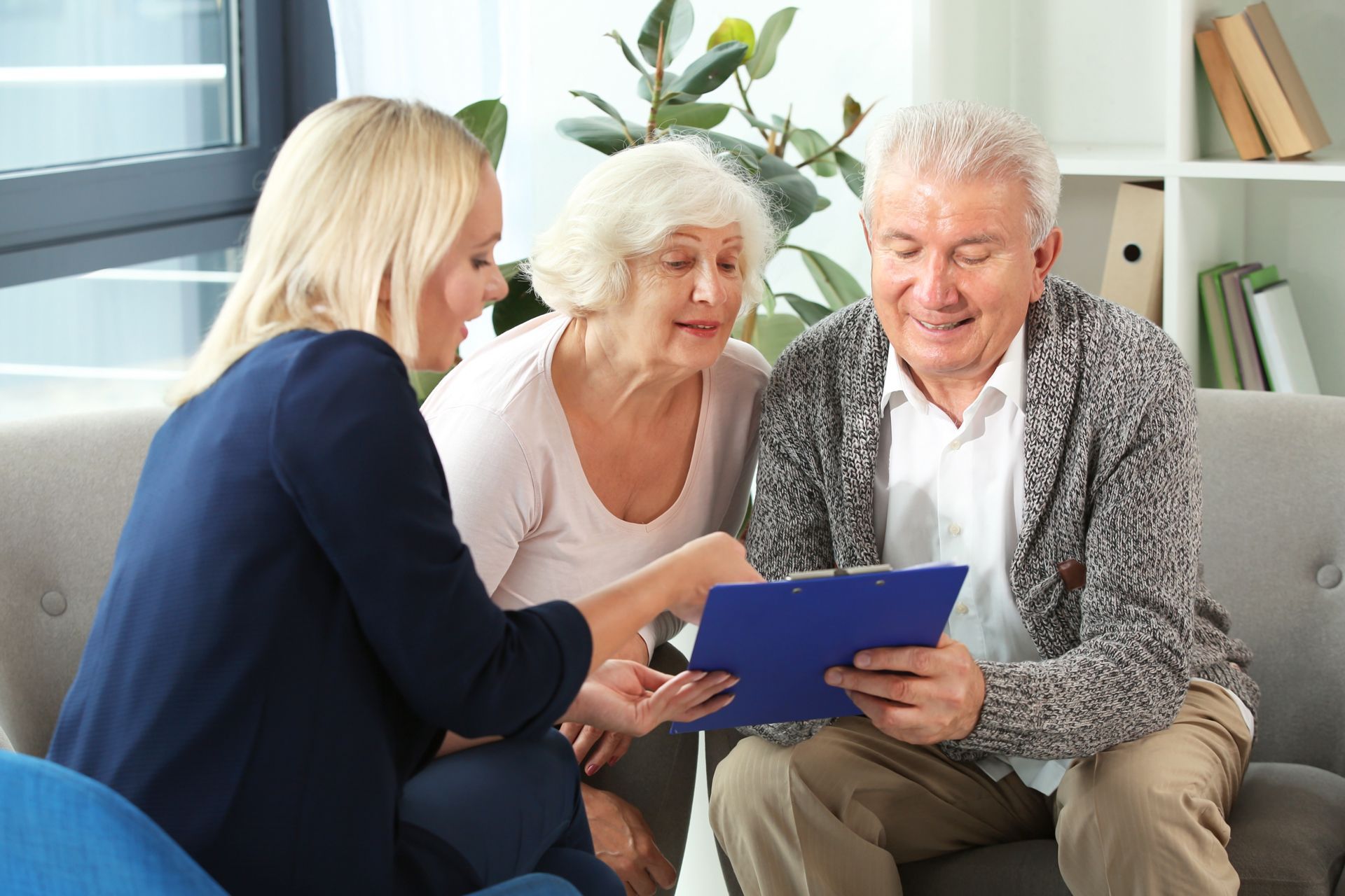 Three people seated on a couch reviewing a tablet together in a bright living room